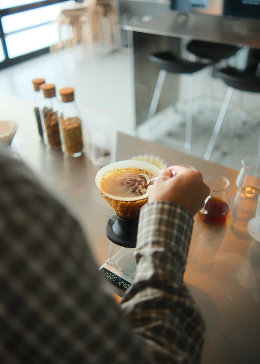 Person making a coffee drink using a coffee machine in a kitchen.